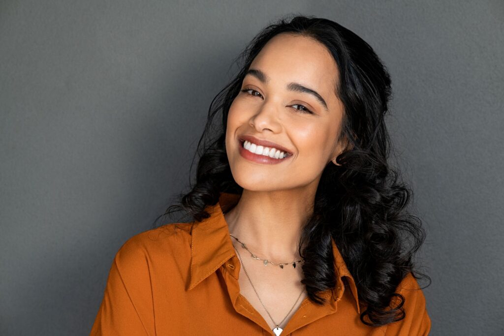 Woman in orange collared shirt smiling in front of grey background